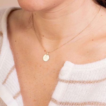 Femme portant un fin collier en or avec un pendentif rond gravé d'un bijou.