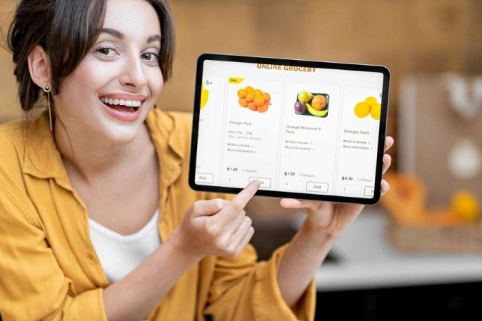 Femme souriante tenant une tablette affichant une boutique numérique, illustrant la facilité d’acheter en ligne.
