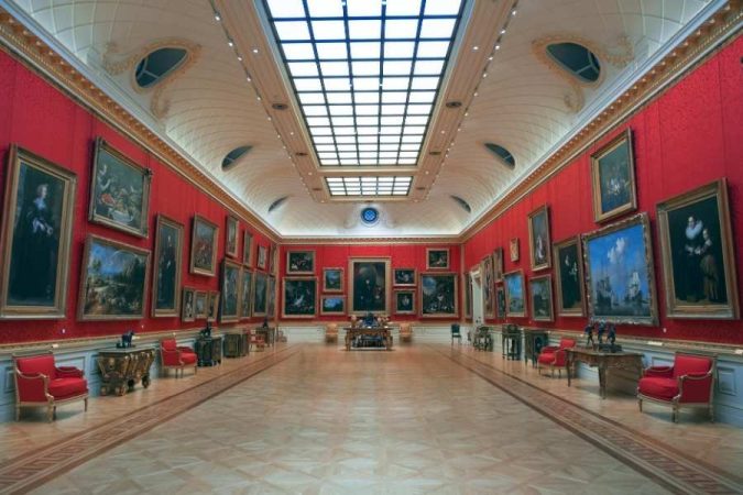 Grande salle d’un musée parisien ornée de murs rouges et de nombreuses peintures anciennes, illustrant des expositions dans les musées parisiens.