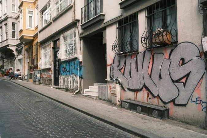 Rue étroite bordée d’immeubles anciens avec un grand graffiti argenté représentant du street art français.