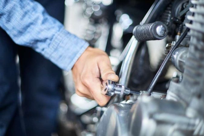 Mécanicien ajustant une pièce de moteur, illustrant une étape essentielle de l’Entretien moto.
