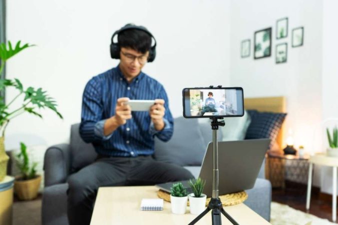 Jeune homme filmant une session de smartphone gaming avec un trépied et un casque audio.