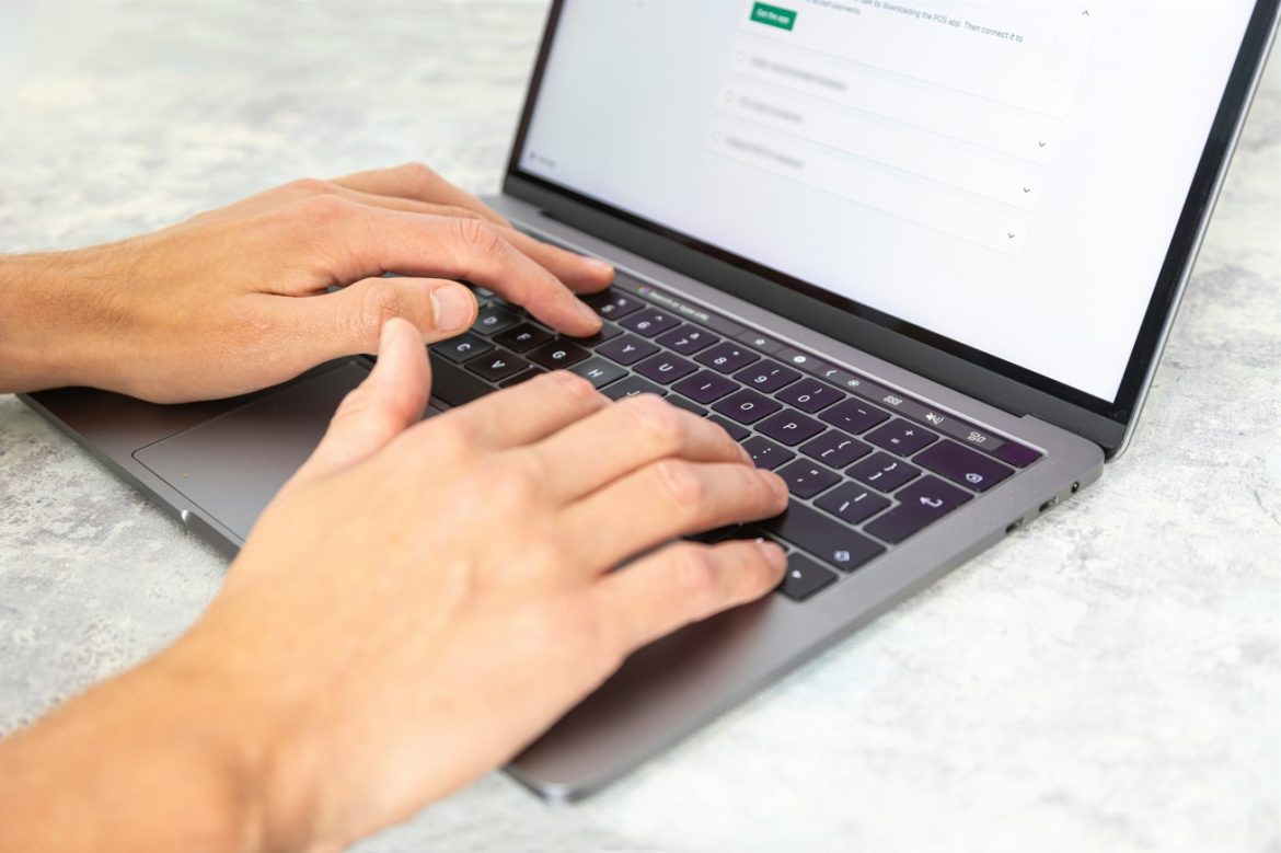 Gros plan des mains d'un chercheur tapant sur le clavier d'un ordinateur portable gris pour utiliser les meilleurs outils IA pour l'analyse des textes anciens et sacrés.