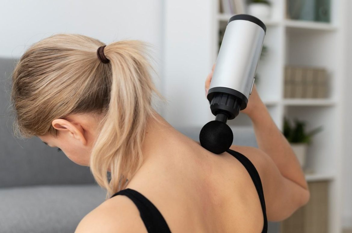 Une femme utilise un pistolet de massage musculaire avec embout boule pour soulager la nuque et le haut du dos.