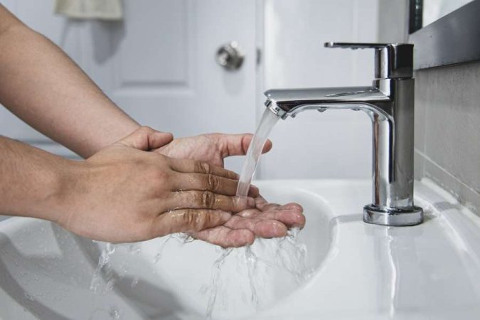 Un gros plan montre des mains qui se lavent sous un jet d'eau coulant d'un robinet mitigeur chromé, dans un lavabo blanc. Un usage responsable de la robinetterie est un premier pas pour réduire sa consommation d'eau.