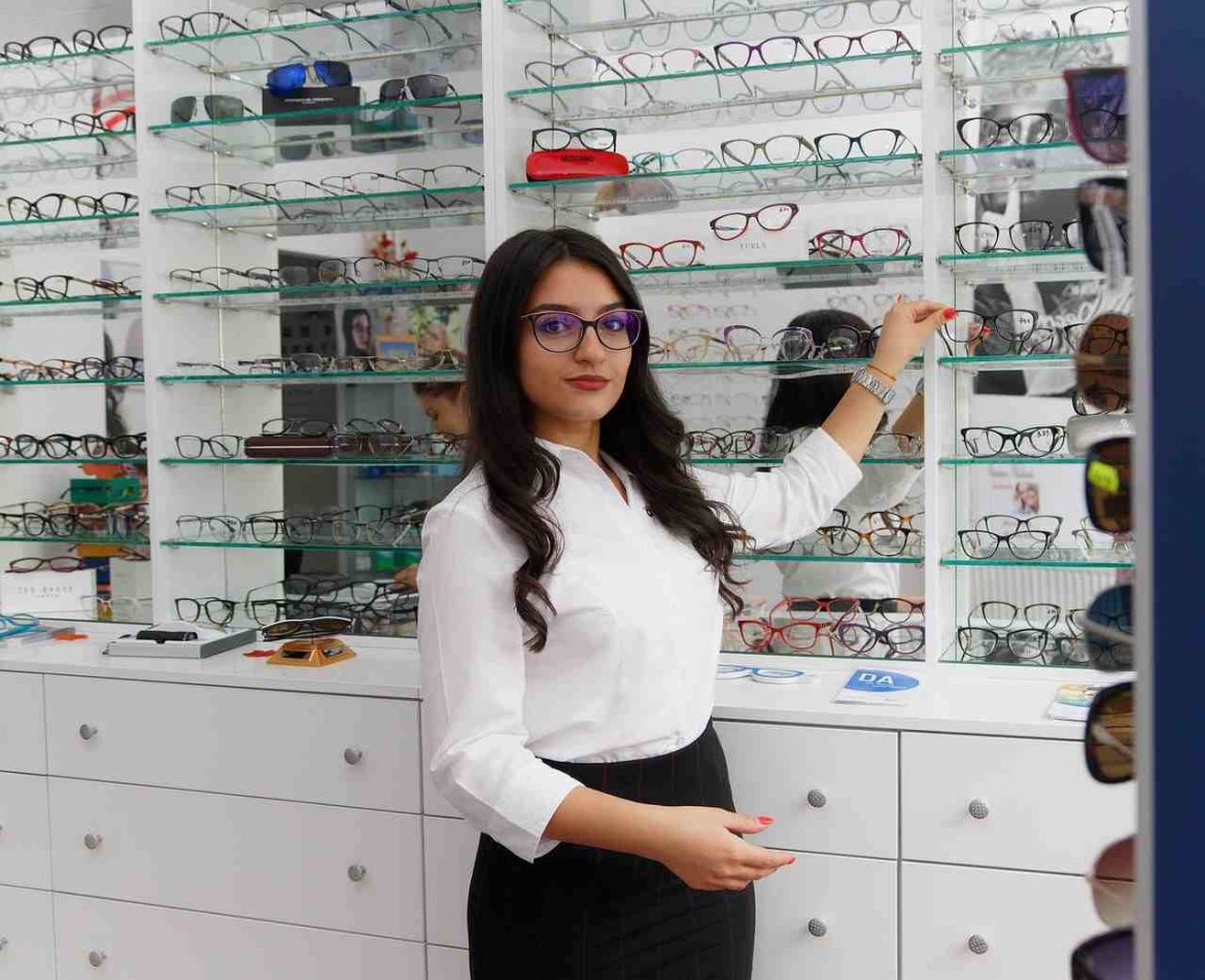 Une opticienne professionnelle dans un magasin d’optique à Reims présentant des lunettes à un client.