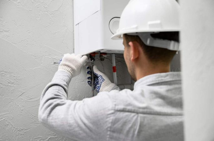 Un technicien en casque de chantier effectue le contrôle d'une chaudière murale pour respecter la loi entretien obligatoire chauffage